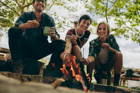 Friends camping in the countryside toasting food on bonfire.