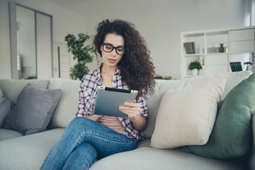 Portrait of her she nice-looking winsome attractive lovely sweet charming cute focused concentrated wavy-haired girl sitting on divan reading ebook in light white interior room