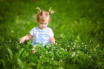 Portrait of adorable little blonde girl lying on grass and propping up her face at summer green...