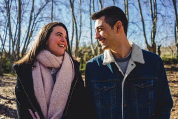 Happy young couple smiling together in a sunny forest on an autumn day.