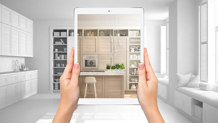 Hands holding tablet showing modern white and wooden kitchen, total blank project background,...