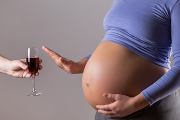 Image of pregnant woman refusing  wine on gray background.