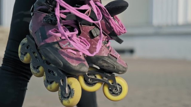 Young woman walk with rollerblades in hands on background of street. Beautiful young girl with roller skates in skate park. Close up view