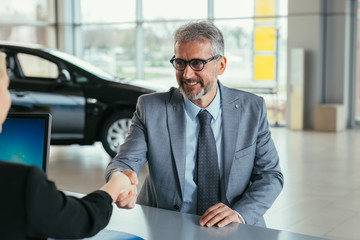 businessman shaking hands with sell agent in car showroom