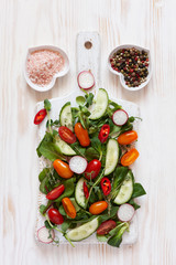 Fresh raw tomatoes, cucumbers, baby spinach and seasonal greens. Top view, close-up on white wooden background.