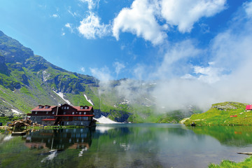 beautiful summer scenery around balea lake. grassy meadows and low clouds around. popular travel destination. location fagaras mountains, romania, europe. wonderful sunny weather