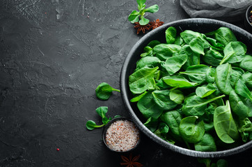 Fresh spinach. In a black plate on a wooden background Top view. Free space for your text. Flat lay