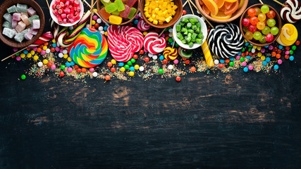 Background of colored candies and lollipops. Sweets. On a black background. Top view. free copying space.