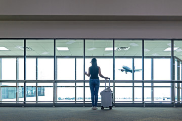 Fototapeta premium Traveler women plan and backpack see the airplane at the airport glass window, Asian tourist hold bag and waiting near luggage in hall airplane departure. Travel Vacation Concept.