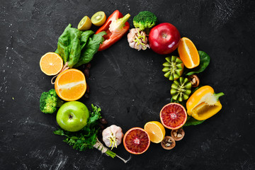 Fruits and vegetables that contain vitamin C: Orange, lemon, apple, roses, garlic, broccoli, apple, kiwi, spinach. Top view. On a black stone background.