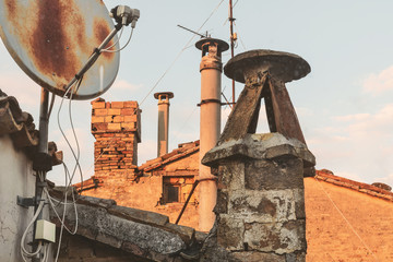 Fototapeta na wymiar Old chimneys and rusty satellite dish, sky on background
