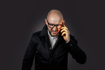 Male businessman with an evil face in a white shirt and dark cloak talks and shouts by telephone on a dark background. Concept stress, bad business, anger, too many phone calls.