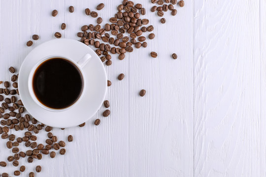 Scattered coffee grains, a cup and black chocolate on a white wooden table. Copy space.