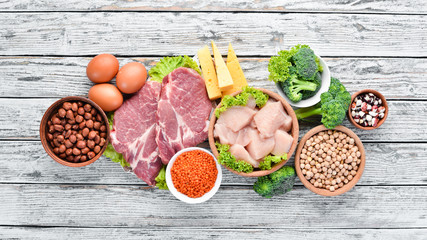 Food high in protein on table. Meat, chicken fillet, broccoli, beans, cheese, eggs, wheat. On a white wooden background.