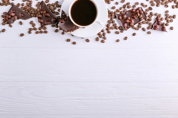 Scattered coffee grains, a cup and black chocolate on a white wooden table. Copy space.