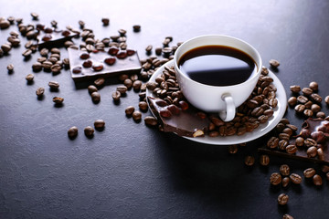 Scattered coffee grains, a cup and black chocolate on a black stone table. Copy space.