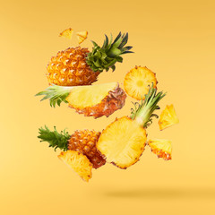 Flying in air fresh ripe whole and cut baby Pineapple with slices and leaves