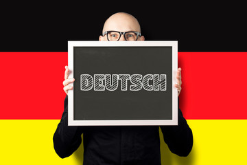 A man in a white shirt and jacket holding a sign with the text deutsch on the background of the flag of Germany. deutsch learning concept, business deutsch.