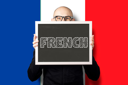 A man in a white shirt and jacket holding a sign with the text French on the background of the flag of France. Concept of learning French, business French.