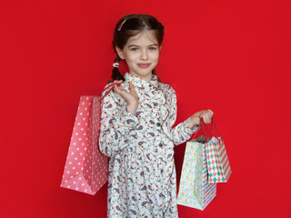 smiling young girl holding a gift bags in her hands on a red background, concept of advertising, sales, discounts