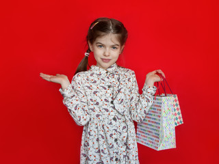 smiling young girl holding a gift bags in her hands on a red background, concept of advertising, sales, discounts