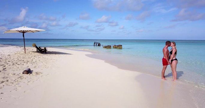 Couple standing in pure Maldives lagoon waters, coming together and kissing, push in then pull back shot 4k