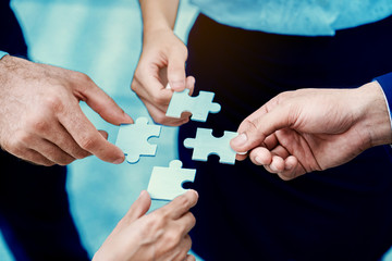Close up at a businessman holding hands. Four puzzles come together. It represents teamwork. Must have understanding in working in the same direction in order to fully and effectively work.