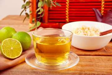 Cooked brown rice in white bowl with chopsticks and cup of green tea on the wooden background.