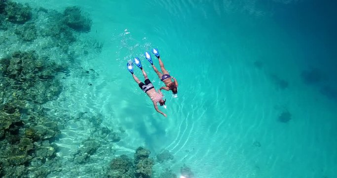 Aerial view around a young couple snorkeling above coral reef reaching deeper parts of the crystal clear water, Maldives.