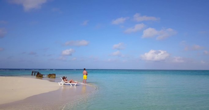 Woman taking photos of man fishing on beautiful island to share on social media, private luxury island