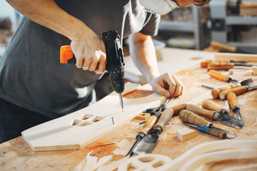 A man carves a tree. The carpenter works with drill in a studio. An engineer provides a tree shape
