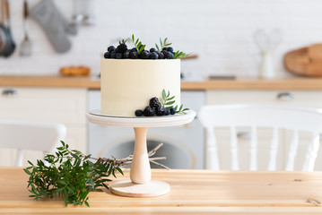 Cake with cream cheese, fresh blueberries and blackberries on the wooden table in the kitchen. Wedding cake, birthday cake on the festive table. Copy space. Close up. Bakery, confectionery concept
