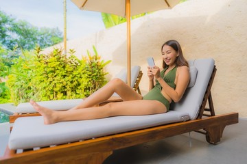 Portrait beautiful young asian woman sitting on the chair deck with umbrella neary swimming pool