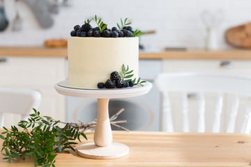 Wedding cake, birthday cake on the festive table. Copy space. Bakery, confectionery concept. Cake with cream cheese, fresh blueberries and blackberries on the wooden table in the kitchen.