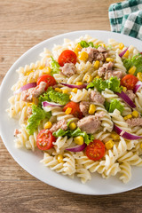 Pasta salad with vegetables and tuna on wooden table. 