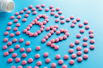 Pink tablets in the form of B12 in the heart on a blue background, spilled from a white can.