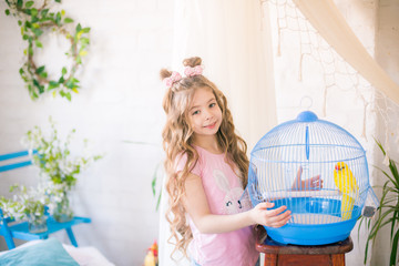Little cute girl with long curly hair with a cage with a yellow parrot at home