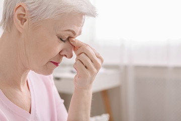 Fatigued senior woman massaging nose bridge, feeling eye strain