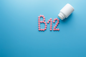 Pink pills in the shape of the letter B12 on a blue background, spilled out of a white can.