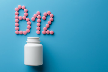 Pink pills in the shape of the letter B12 on a blue background, spilled out of a white can.
