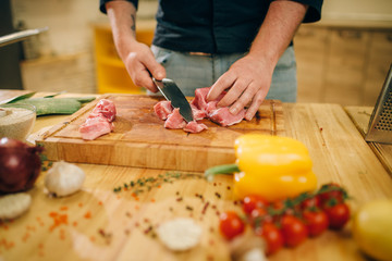 Male person cuts raw meat into slices, top view