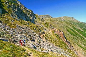Summer mountain scene, hiking tourists on trail.