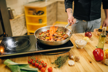 Male chef cooking meat with vetables on fire