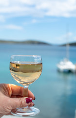 hand with glass of white wine served outside on balcony with sea view