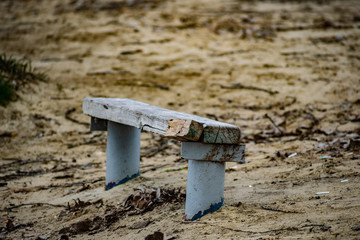 Small wooden old bench, with peeling paint in the sand on the beach among nature and trees