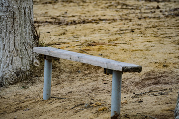 Small wooden old bench, with peeling paint in the sand on the beach among nature and trees