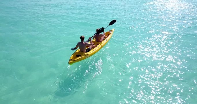 A young couple paddles their kayak through beautiful water in the Bahamas. Camera tilts up to follow them to reveal the horizon. Aerial, tilt, 4k.