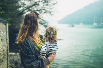 Young mother with toddler in sling by river
