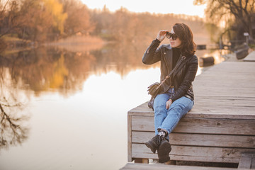 young pretty fashion woman sitting on pier on sunset with beautiful view of river