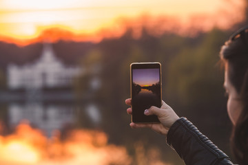 woman taking picture of sunset on her phone